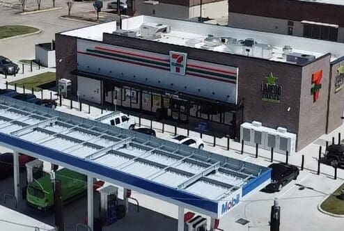 A gas station with a large roof and several cars parked on the side.