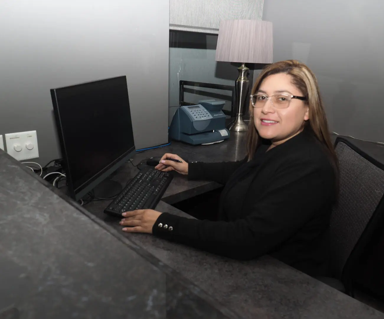 A woman sitting at the computer desk in front of a laptop.